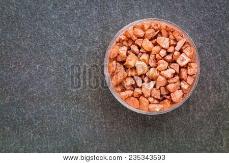 Crystals of traditional Hawaiian alaea sea salt containing red vocanic clay, a small bowl agains gray slate rock with a copy space