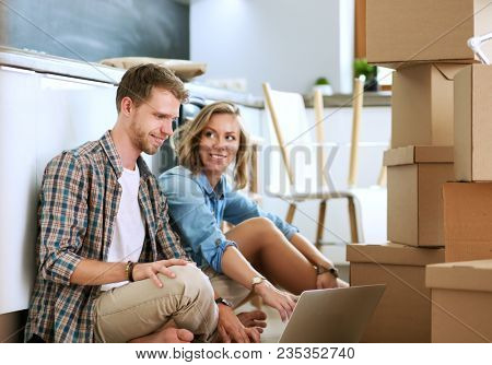 Young couple moving in new home.Sitting and relaxing after unpacking.Looking something on laptop. Young couple