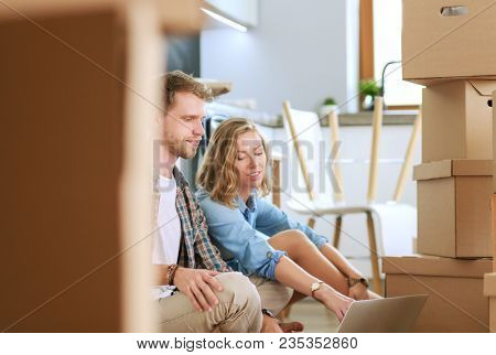 Young couple moving in new home.Sitting and relaxing after unpacking.Looking something on laptop. Young couple