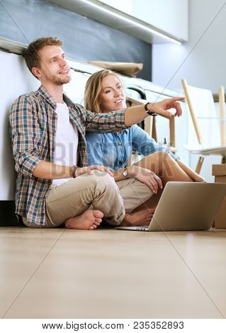 Young couple moving in new home.Sitting and relaxing after unpacking.Looking something on laptop. Young couple