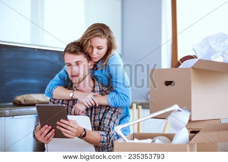 Young couple moving in new home.Sitting and relaxing after unpacking.Looking something on laptop. Young couple