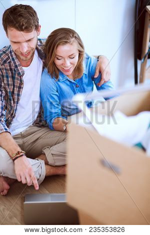 Young couple moving in new home.Sitting and relaxing after unpacking.Looking something on laptop. Young couple