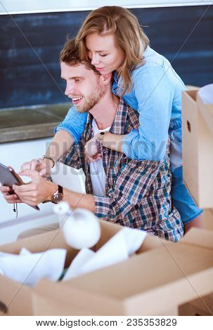 Young couple moving in new home.Sitting and relaxing after unpacking.Looking something on laptop. Young couple
