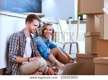 Young couple moving in new home.Sitting and relaxing after unpacking.Looking something on laptop. Young couple