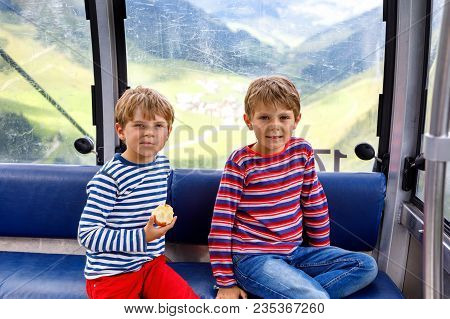 Two Little Boys Sitting Inside Of Cabin Of Cable Car And Looking On Mountains Landscape. Family On H