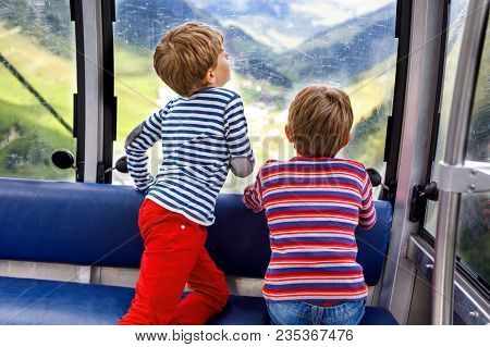 Two Little Boys Sitting Inside Of Cabin Of Cable Car And Looking On Mountains Landscape. Family On H