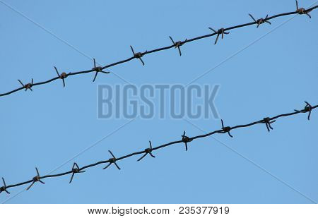 Old Rusty Mono-basic Barbed Wire In Two Lines On A Clear Blue Sky