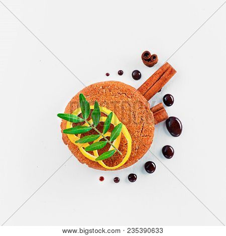 Cookie Decorated With Lemon Zest, Chocolate Drops, Cinnamon, And Green Leaves On A White Background.