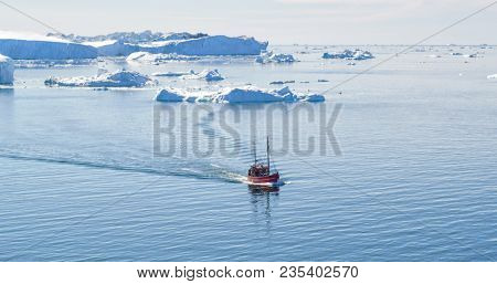 Icebergs and tourist fishing boat in Greenland iceberg landscape of Ilulissat icefjord with giant icebergs. Icebergs from melting glacier. Aerial drone photo of arctic nature.