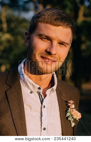Young Groom Looks At Camera And Smiles Against Nature Background