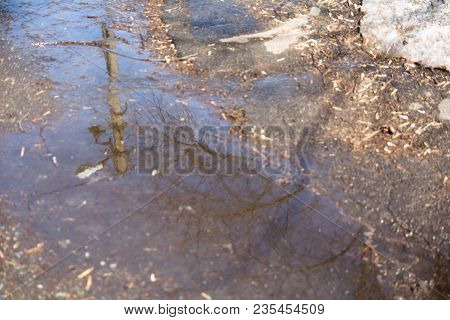 Ripples And Reflections In A Spring Puddle And Melting Snow In City