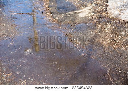 Ripples And Reflections In A Spring Puddle And Melting Snow In City