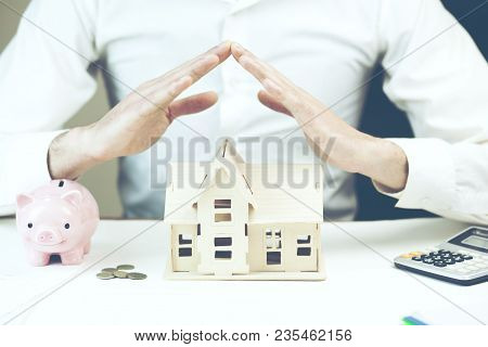Man Protecting His House With Calulator And Piggy Bank On Table