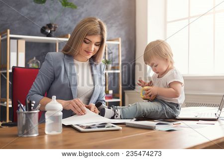 Happy Beautiful Business Mom Working With Documents In Office While Her Cute Baby Playing With Toys.