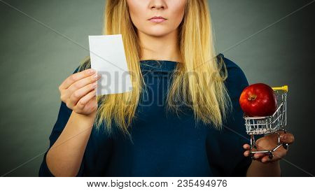 Worried Woman Holding Shopping Basket With Fruits Looking At Bill Receipt Being Scared Of Huge Price