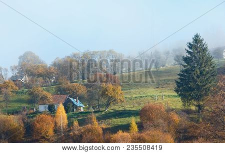 Autumn Carpathian Mountains Landscape With Multicolored Trees And Small Hamlet On Slope, And Misty C