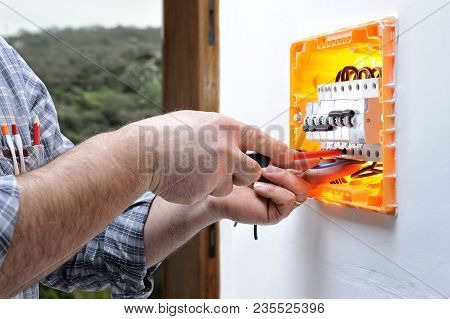 Electrician Technician At Work On A Residential Electric Panel, He Fixes The Wire With The Screwdriv