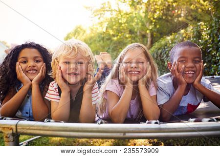 Four kids lying down together on a trampoline in the garden