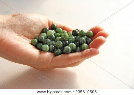 Natural Green Jade Nephrite Mineral Stones Beads. The Green Jade Stone Lies In The Hands. Hands Hold