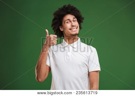 Photo of hansome young african curly man standing isolated over green wall background showing thumbs up gesture.