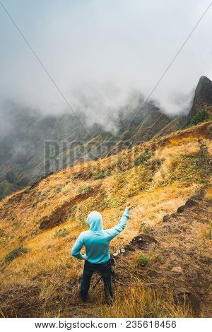 Traveler Staying On The Cobbled Path And Admiring Clouds Flowing Over The Mountain Peaks Into The Va