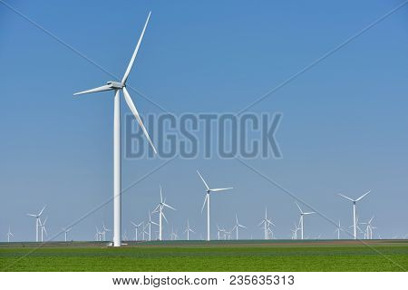 Eolian Farm Renewable Energy In Fresh Green Field Against Clear Blue Sky