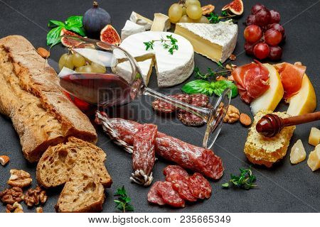 Various Types Of Cheese, Meat, Fruits And Wine On Dark Concrete Background