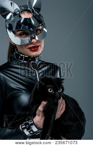 Kinky Woman In Sexy Costume And Mask Holding Black Cat Isolated On Grey