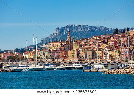 View of small harbor with yachts and old colorful houses of the Old Town on background in Menton - popular tourist resort on French Riviera.