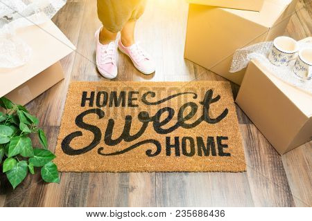 Wman in Pink Shoes and Sweats Standing Near Home Sweet Home Welcome Mat, Boxes and Plant.