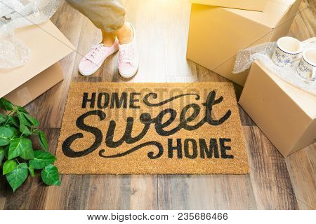 Wman in Pink Shoes and Sweats Standing Near Home Sweet Home Welcome Mat, Boxes and Plant.