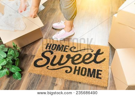 Wman in Pink Shoes and Sweats Unpacking Near Home Sweet Home Welcome Mat, Moving Boxes and Plant.