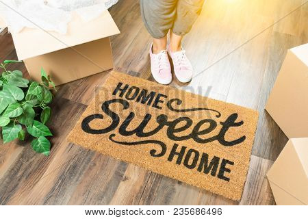 Wman in Pink Shoes and Sweats Standing Near Home Sweet Home Welcome Mat, Boxes and Plant.