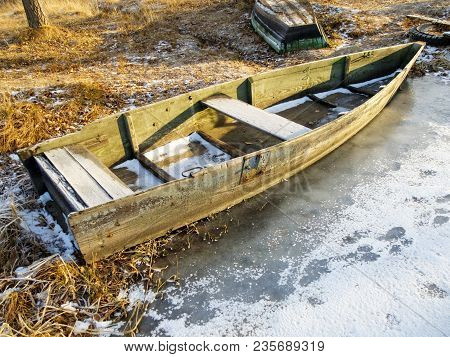Old Boat On The Shore Frozen Into The Ice In Autumn.