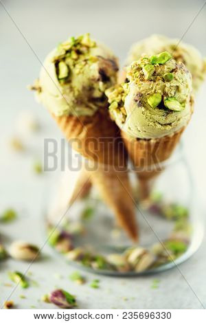 Green Ice Cream In Waffle Cone With Chocolate And Pistachio Nuts On Grey Stone Background. Summer Fo