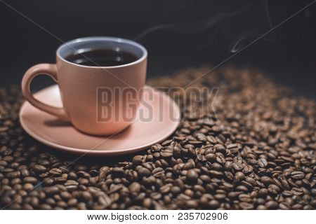 Cup Of Black Steaming Coffee On A Spilled Roasted Coffee Beans On A Black Background.