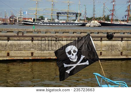 Black Pirate Flag Flying Form The Top Of A Mast On A Boat In The Port