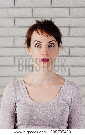 A Pretty Girl With Surprised Face, Wide Opened Eyes, With White Brick Wall In The Background. Face M