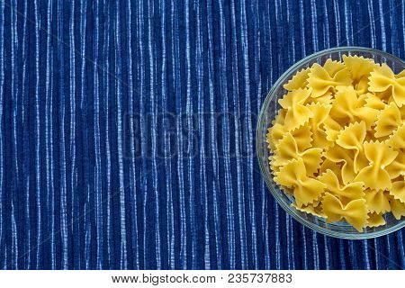 Farfalle Raw Pasta In A Glass Cup On A Striped White Blue Cloth Background With A Side. Close-up Wit