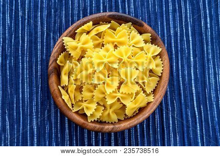 Farfalle Raw Pasta In A Wooden Bowl On A Striped White Blue Cloth Background In The Center. Close-up