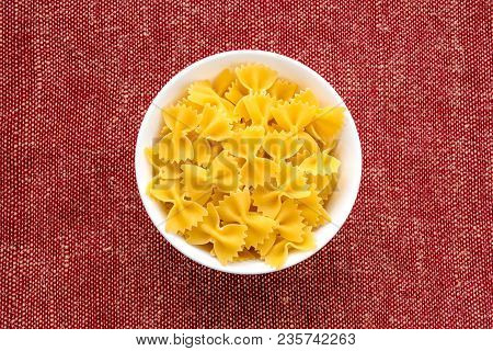 Farfalle Raw Pasta In A White Cup On A Red Brown Rustic Texture Background, In The Center Close-up F