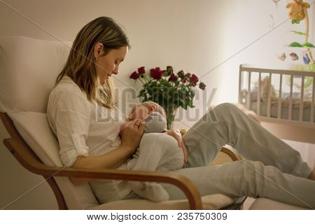Young Beautiful Mother, Breastfeeding Her Newborn Baby Boy At Night, Dim Light