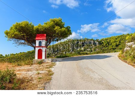 Little Chapel And Pine Tree Near The Sphalt Road Of Zakynthos Island In Sunny Summer Day. Greece