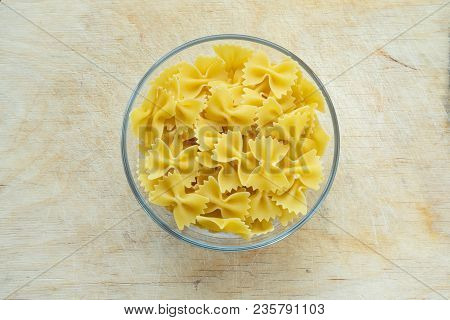 Farfalle Raw Farfallini Pasta In A Glass Bowl On A Wooden Table Texture Background, In The Center Wi
