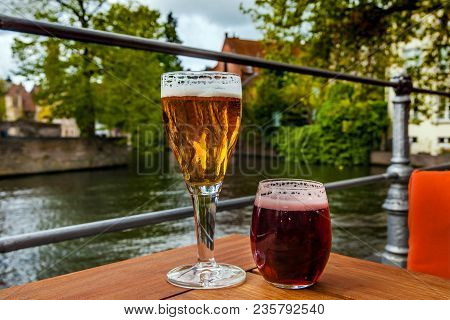 Two Glasses Of Belgian Beer Standing On The Table With Bruges City View