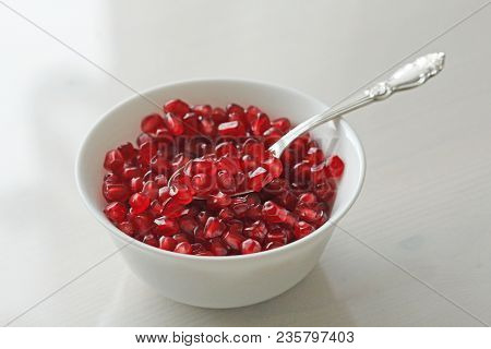 Grains Of Red Ripe Pomegranate Lie In A White Bowl With A Spoon. Big Ripe Red Granets Or Garnets. Fr