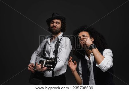 Duet Of Expressive Musicians Playing Acoustic Guitar And Harmonica On Black