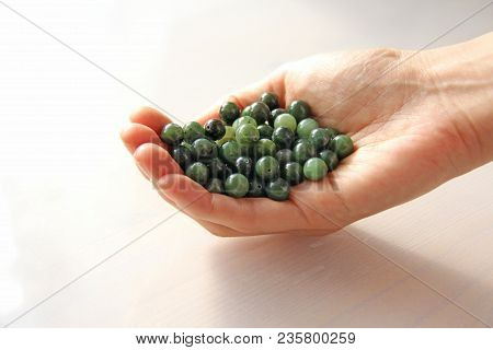 Natural Green Jade Nephrite Mineral Stones Beads. The Green Jade Stone Lies In The Hands. Hands Hold