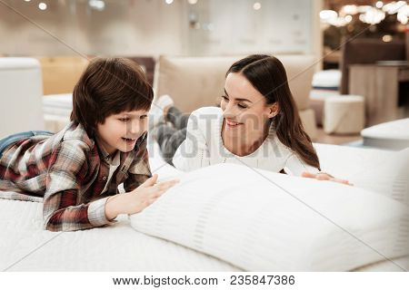 Young Beautiful Woman With Cute Little Boy Lies On Bed In Mattress Store. Family Checking Softness O