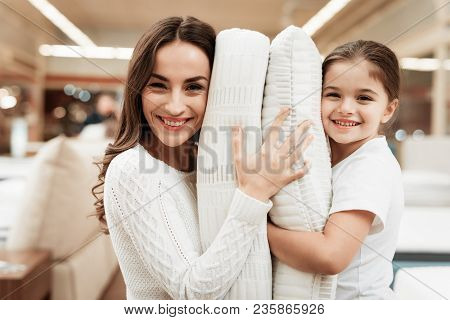 Smiling Little Girl With Beautiful Mother Hugs Pillows In Store Of Orthopedic Mattresses. Testing So